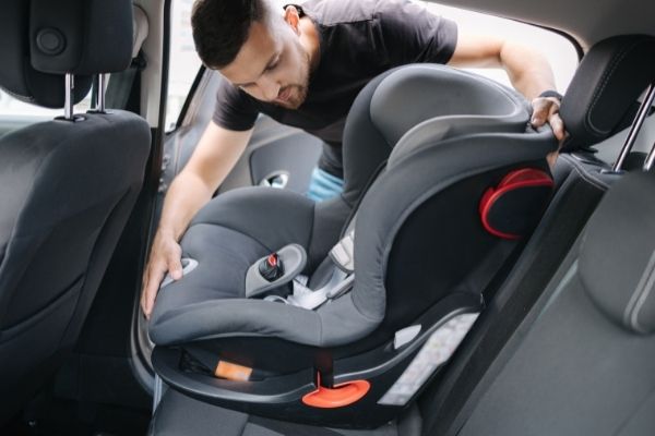 Man installing a child seat in a rental car. Include a child seat when you rent a car in Ericeira 