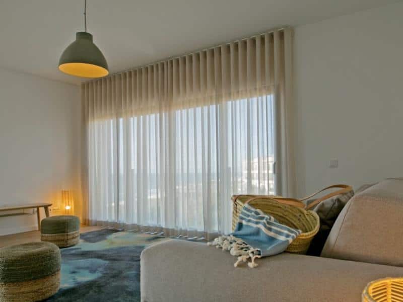 A straw bag on a couch placed by a window with a view to the seaside at You and the sea boutique hotel Ericeira.