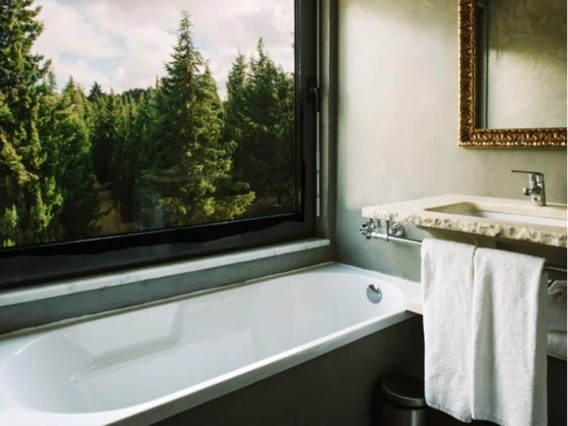 An old fashioned bathtub placed by a window with a beautiful forest view. This is one of the bathroom at Quinta dos Machados Boutique Hotel right outside of Ericeira.