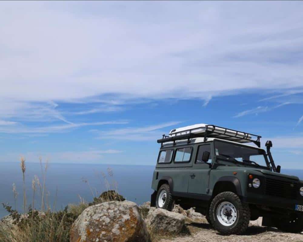 A Landrover Jeep perched on a rocky cliff above the sea.