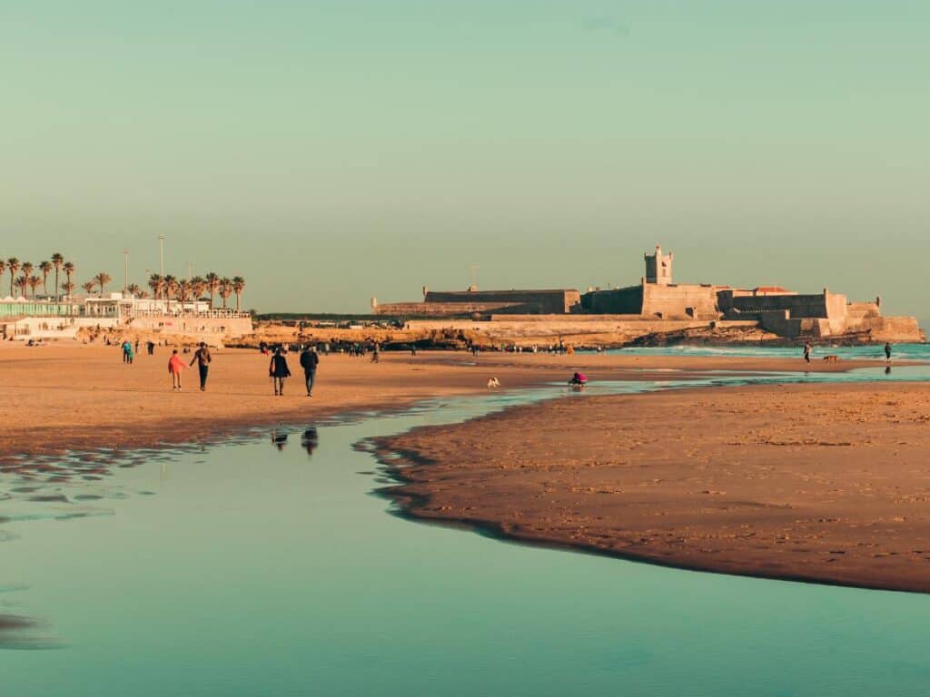 Carcavelos in winter at low tide at the end of the day. The fort in the background and restaurants to the left of the beach.