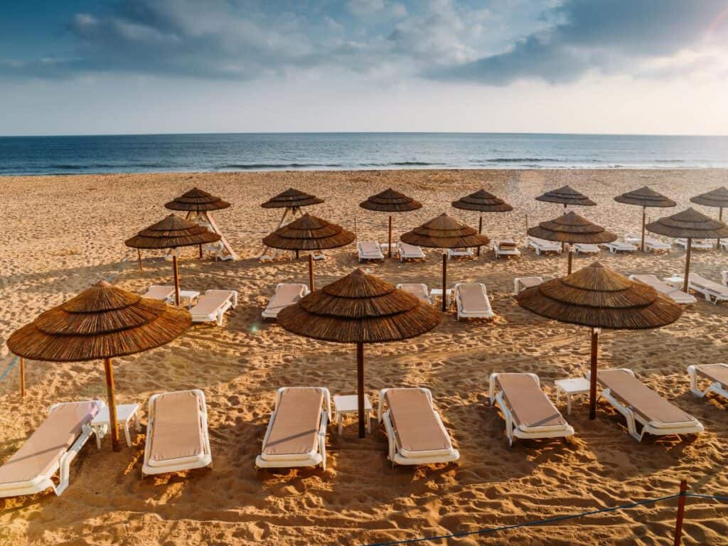beach loungers and shades set up on the beach in Costa da Caparica. on the beautiful sand, the blue water and a bright cloudy day.