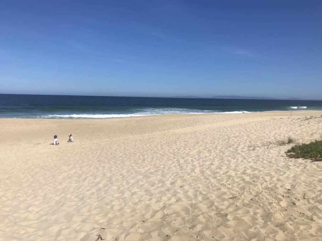 The golden sand goes on forever on the Costa da Caparica. Two children playing in the sand with the blue sea in the distance.