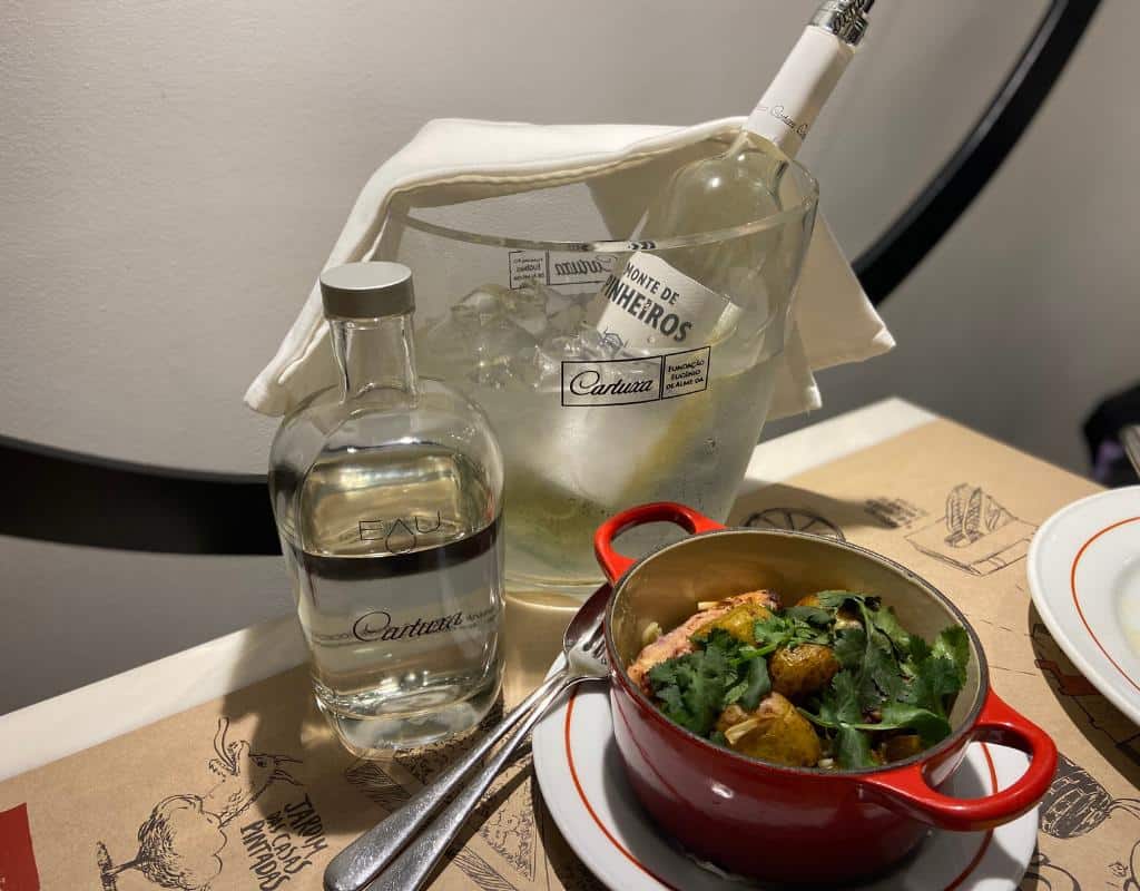 White wine put on ice as well as a bottle of water and polvo a lagareiro dish served in red crockery as served at Cartuxa winery. What to do in Evora Portugal? Eat, drink, and be merry!