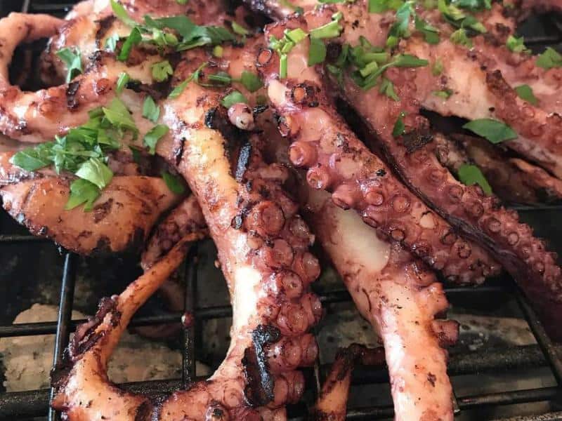 Plate of octopus done on the grill with some parsely on top. 