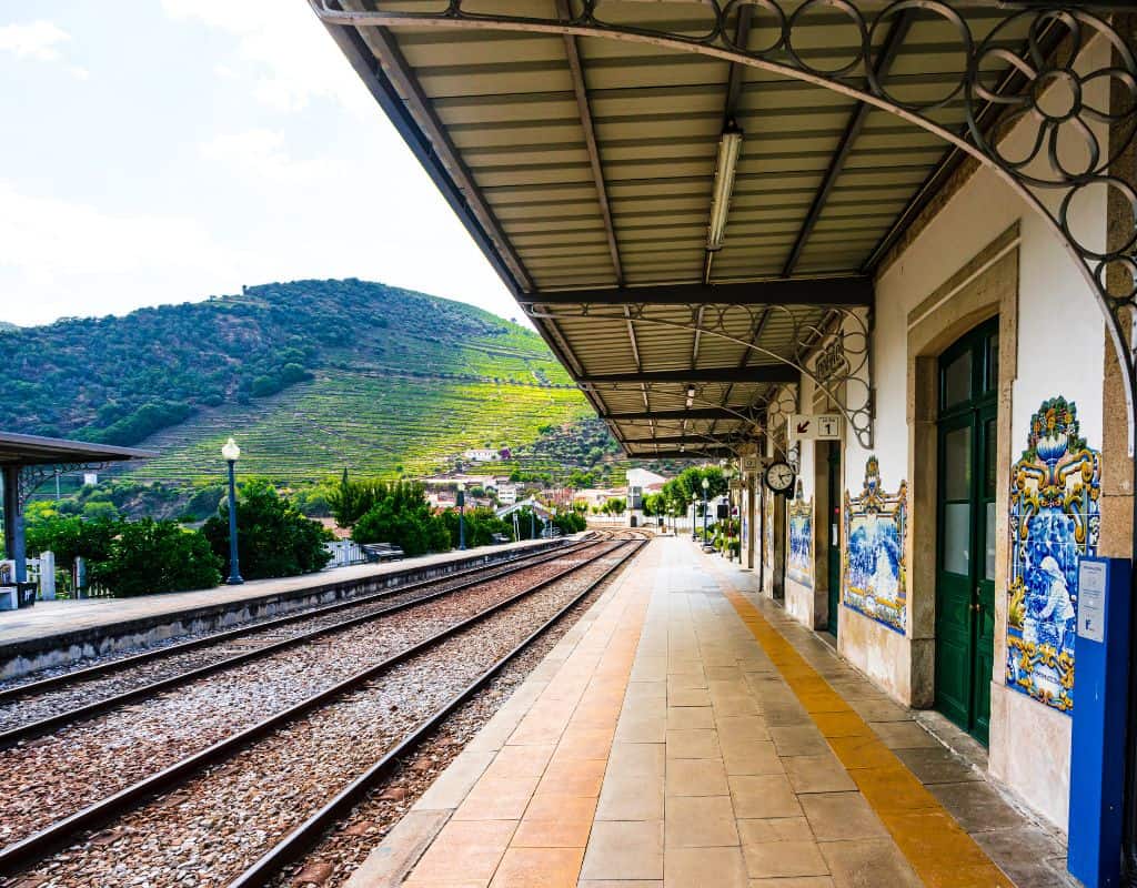 The Peso da Regua scenic train station platform with colorful tile murals, nestled against a backdrop of lush green hills and terraced vineyards, illustrating the route from Porto to Douro Valley by Train.
