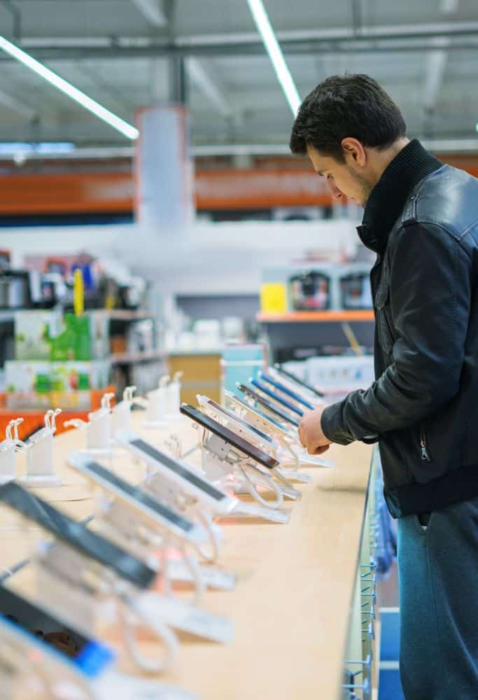 A man looks at a display of phones in a tech store, possibly considering purchasing a new Portugal SIM Card compatible smartphone.