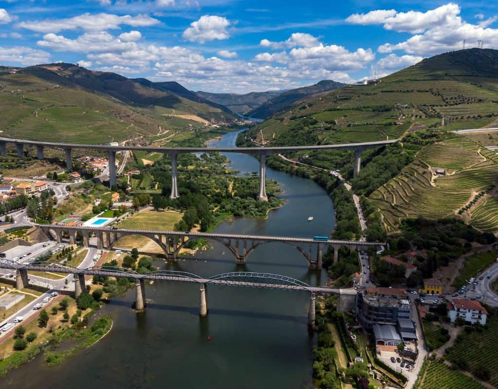 Aerial view of the Douro Valley with its expansive vineyards, winding river, and multiple bridges connecting the region. This picturesque landscape is part of the scenic Porto to Douro Valley by Train journey.