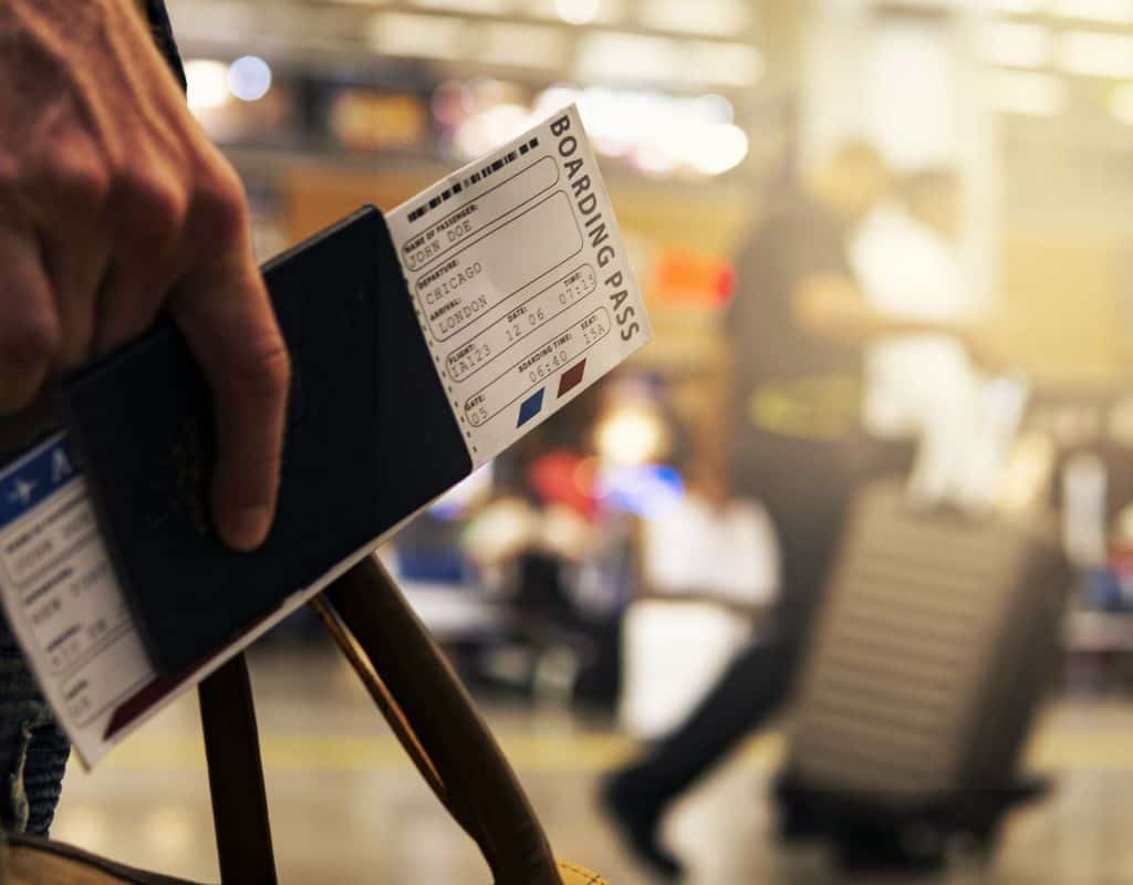 Close-up of a hand holding a passport and boarding pass, ready for boarding at an airport, with luggage and travelers blurred in the background.